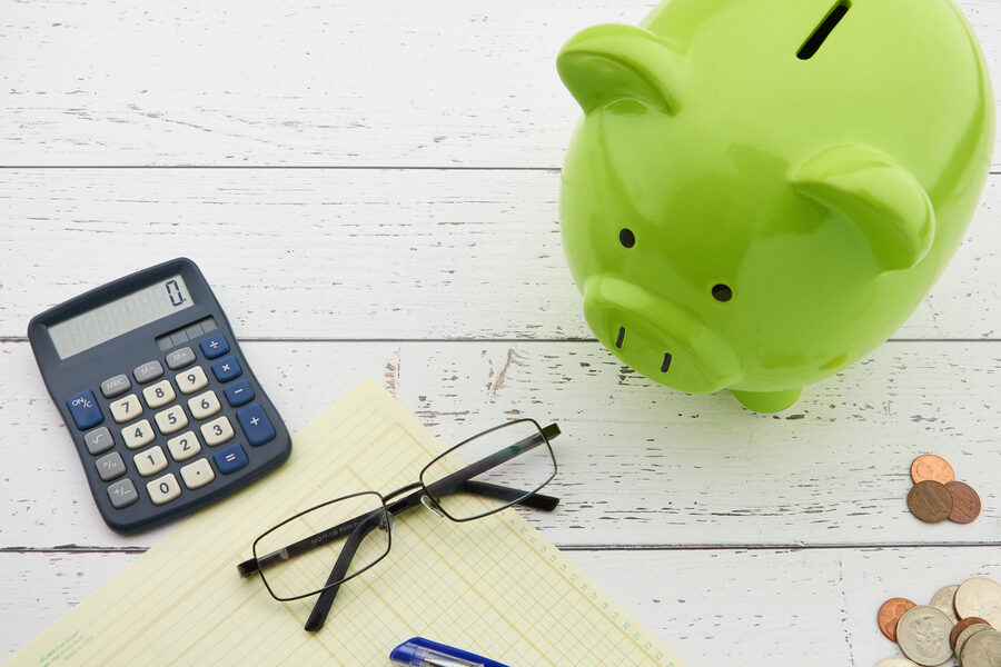 Tirelire, calculatrice et bloc-notes posés sur un bureau clair